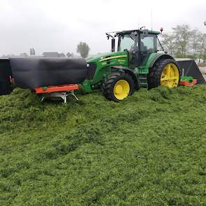 Op de bult rijdt een trekker met verdeler en wals het gras aan. De wals zorgt ervoor dat het gras flink wordt aangedrukt.