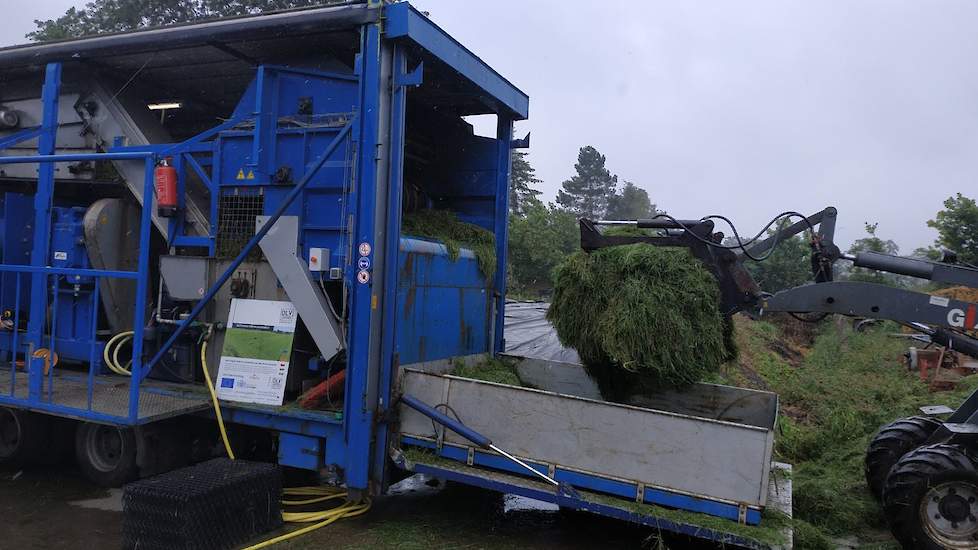 Melkveehouder Jan Veenstra heeft een wagen vers gras gemaaid. Met een shoveltje wordt gras aan de achterkant van de installatie in een voorraadbak gedeponeerd. Veenstra is zelf niet direct bij het project betrokken. Het feit dat zijn bedrijf is gekozen al