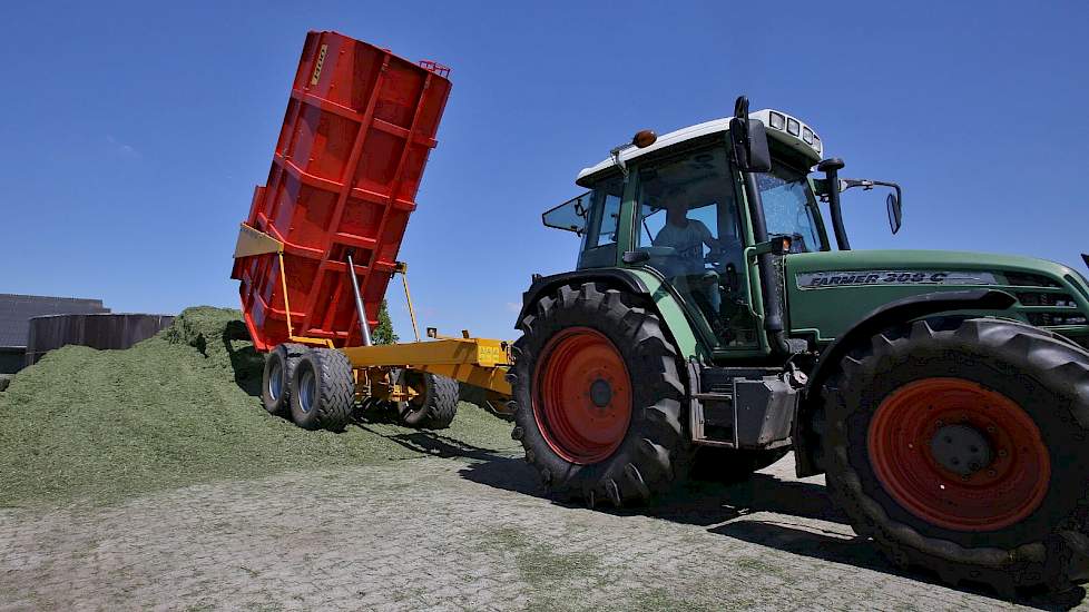 Twee wagens rijden het gras van het veld naar de silo.