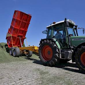 Twee wagens rijden het gras van het veld naar de silo.