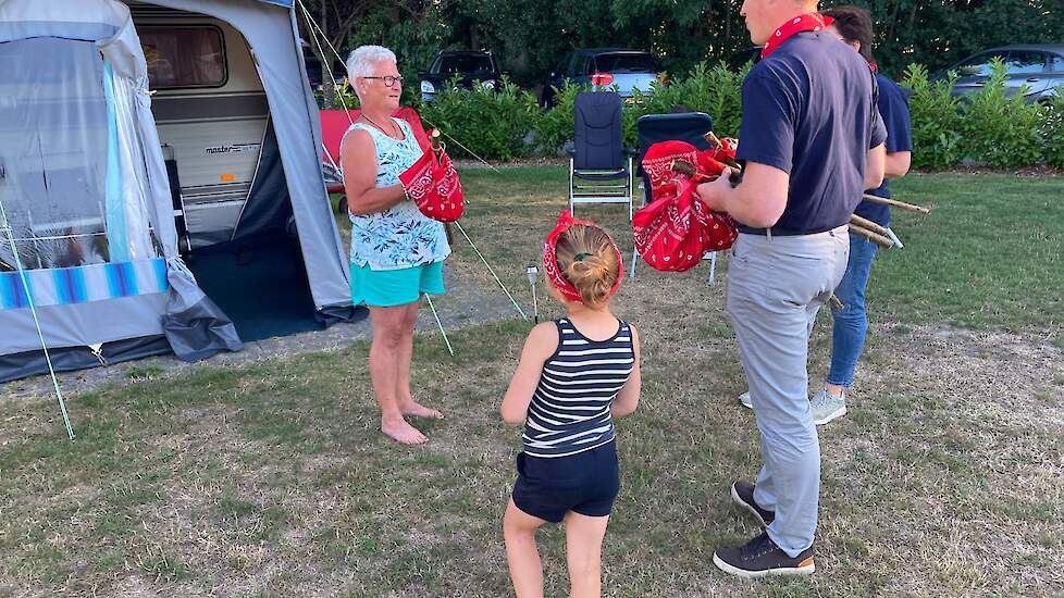 Kamphuis en Vedders bieden een knapzak aan bij een campingbezoeker. Deze wordt met sympathie in ontvangst genomen.