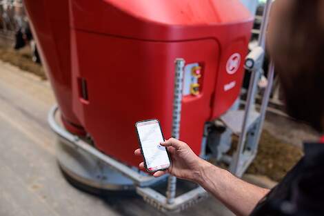 Lely Horizon app die aanstaat op de telefoon met op de achtergrond een voerrobot