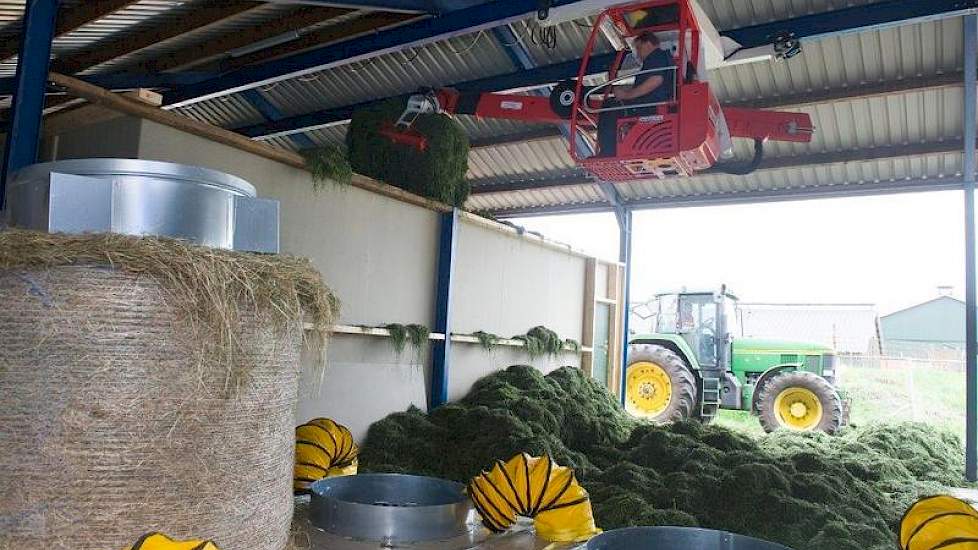 Henk Snuverink laadt met behulp van de halkraan het voorgedroogde gras in de droogbak. Op de voorgrond is het balendroogsysteem met grondbakbeluchting te zien.