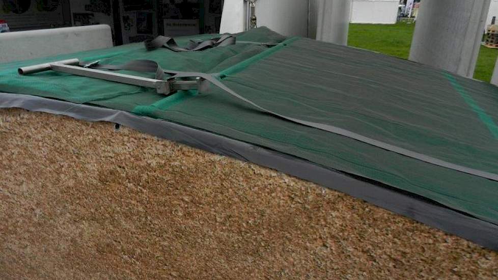MBS-beton presenteert haar nieuwe ‘Silage Safe' afdeksysteem. Aan weerszijden worden om de twee meter stroken kunststof doek gelegd. Aan de linkerkant zit een spanband en aan de rechterkant een stalen buis. Door de spanbanden aan te trekken worden de twee